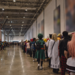 Fila de fãs fantasiados no corredor do Anhembi durante o Anime Friends, aguardando entrada em um estande.