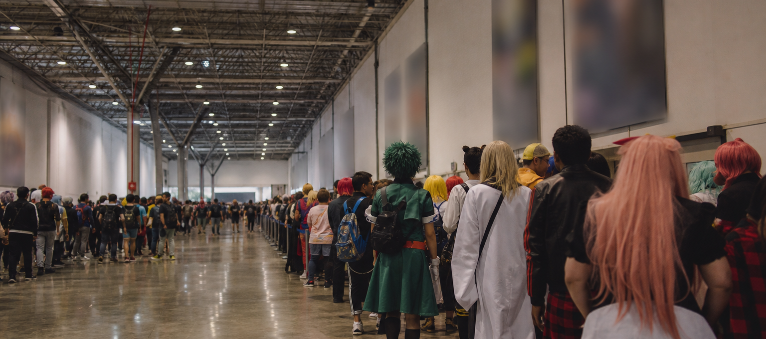 Fila de fãs fantasiados no corredor do Anhembi durante o Anime Friends, aguardando entrada em um estande.