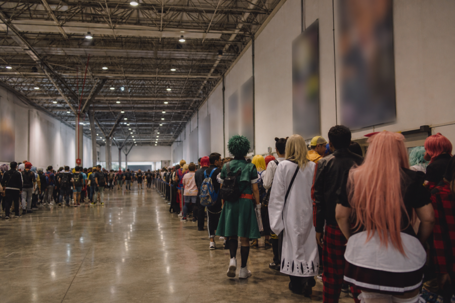 Fila de fãs fantasiados no corredor do Anhembi durante o Anime Friends, aguardando entrada em um estande.