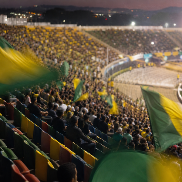 Arquibancadas cheias com bandeiras verde e amarelo em um estádio, sem marcas visíveis.