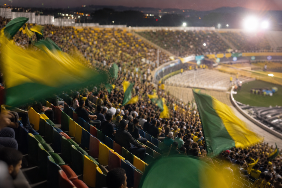 Arquibancadas cheias com bandeiras verde e amarelo em um estádio, sem marcas visíveis.