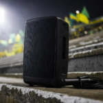 Arquibancada com bandeiras ao fundo e caixa de som apoiada no degrau, luzes de estádio ao anoitecer
