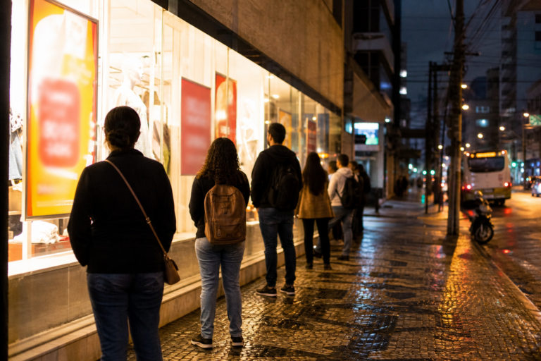 Vitrine iluminada e fila discreta na calçada durante grande promoção, sem marcas visíveis.