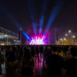 Palco iluminado e público de costas em festival no Rio de Janeiro.