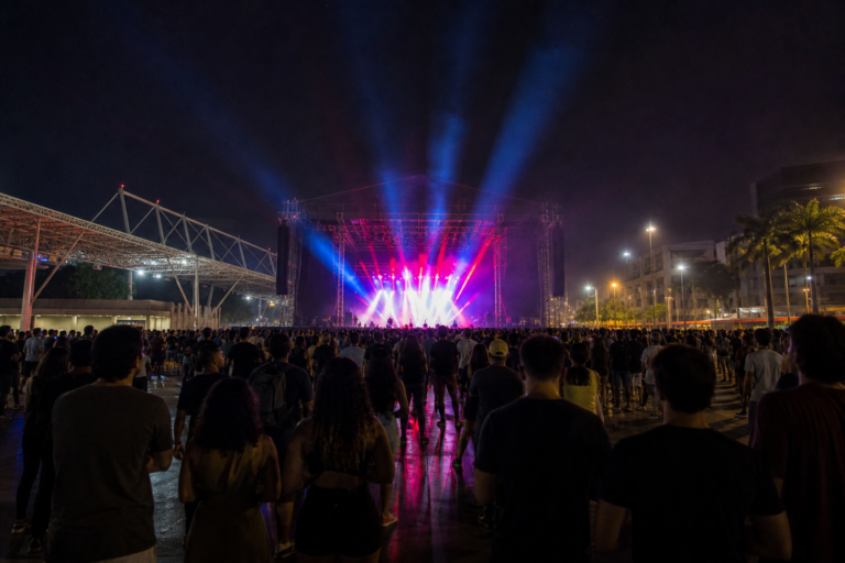 Palco iluminado e público de costas em festival no Rio de Janeiro.