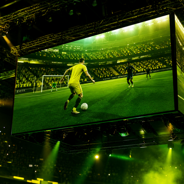 Telão de eSports com avatar de futebol e luzes verde e amarelas diante de arquibancada lotada, sem marcas visíveis.