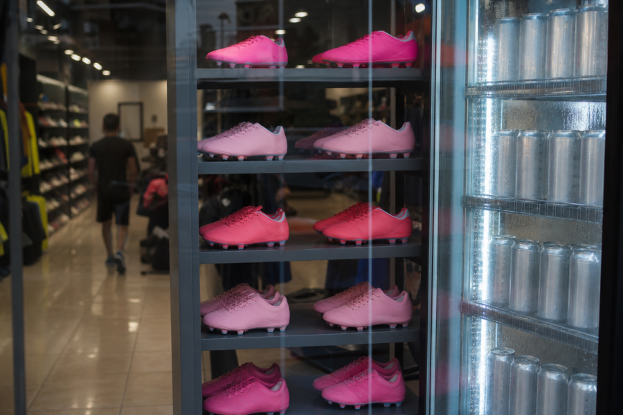 Vitrine de loja com chuteiras rosas e prateleira de bebidas zero sem rótulo, sem marcas visíveis.
